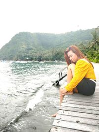 Portrait of woman sitting by lake against sky