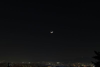 Crescent moon over illuminated city against sky at night