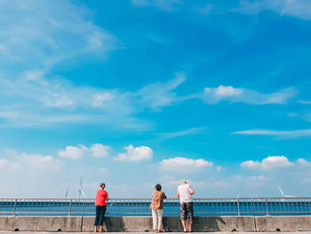 Rear view of people standing at water basin against sky