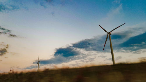 Low angle view of windmills on field against sky