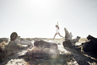 Woman jumping on driftwood during sunny day