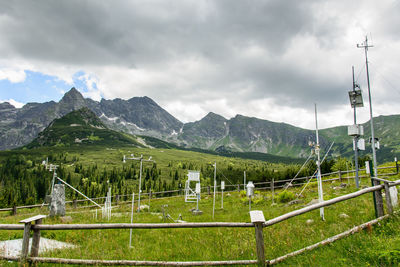 Fence on field at weather station against cloudy sky