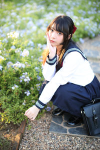 Portrait of young woman crouching by plants outdoors