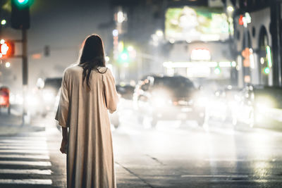 Rear view of mysterious woman on city street at night