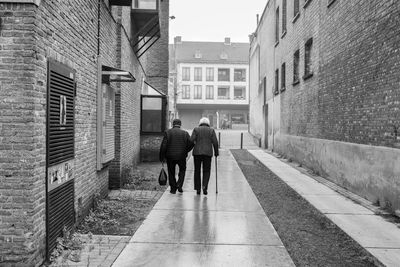 Rear view of people walking on footpath amidst buildings