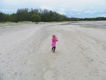 Side view of girl standing at beach against cloudy sky