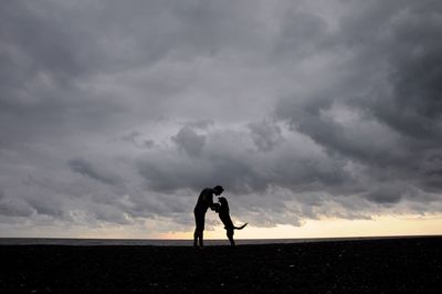 Silhouette man with dog standing on land against sky during sunset