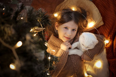 Cozy girl and domestic cat are under the christmas tree, dark golden style. 