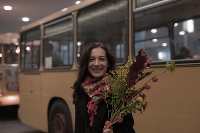 Portrait of woman holding bouquet while standing against bus on road at night