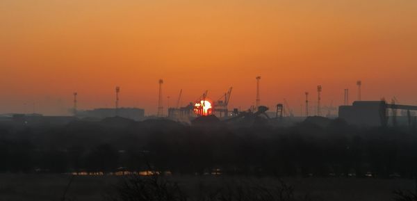 Silhouette factory against orange sky