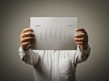 Man holding calendar in front of face while standing against gray background