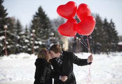 Rear view of couple holding red balloons