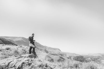 Side view of backpack man standing on mountain against clear sky