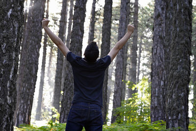 Rear view of man standing by tree trunk in forest