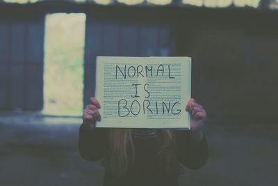 Close-up of woman covering face with book while standing outdoors