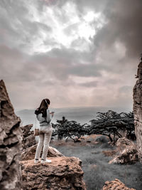 Man standing on rock by sea against sky