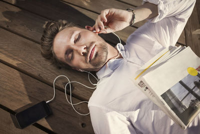 High angle view of businessman listening music while lying on boardwalk