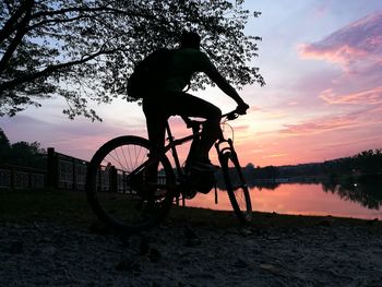 Low angle view of silhouette man riding bicycle at lakeshore