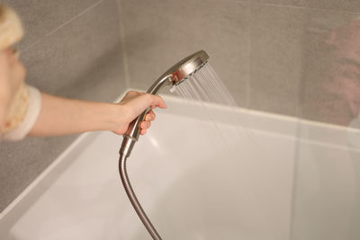 Woman turned on the shower, holding a shower head by hand