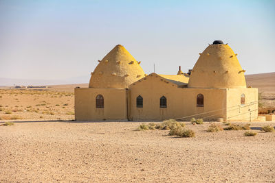 A unique earthen architectural structure located in an isolated desert area under clear skies.