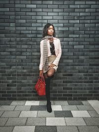 Full length of woman standing against black brick wall