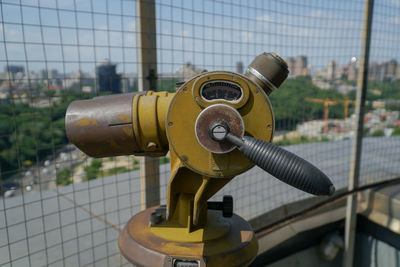 Close-up of vintage coin-operated binoculars against chainlink fence in city