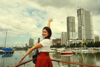Portrait of smiling young woman standing on city against sky