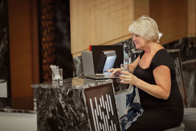 Side view of woman using mobile phone while sitting on table