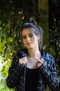 Portrait of young woman standing against tree