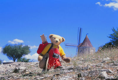 Stuffed toy on field against clear blue sky