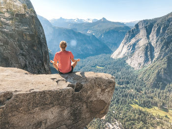 Rear view of woman meditating while sitting on rock