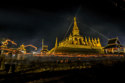Illuminated temple by building against sky at night