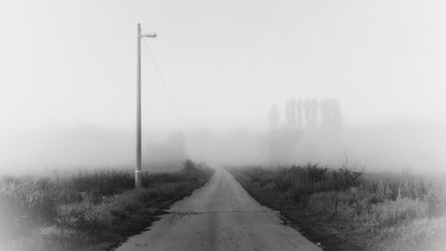 Road amidst trees against sky during foggy weather