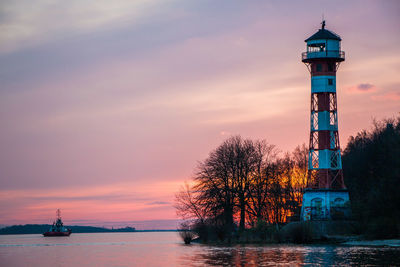 Lighthouse by sea against sky during sunset