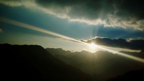 Sunlight streaming through silhouette mountains against sky