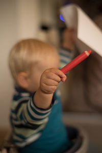 Close-up boy holding red colored pencil and paper with arms raised