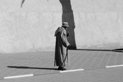 Side view of man walking on footpath against wall