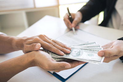 Cropped hands of businessman bribing male coworker at desk in office