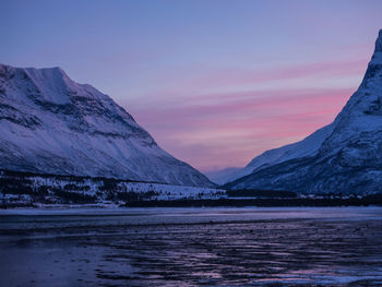 Scenic view of lake by snowcapped mountains against sky during sunset
