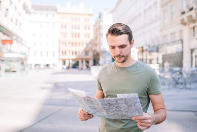 Portrait of young man holding map while standing in city