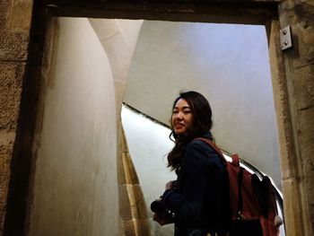 Young woman looking away while standing against wall