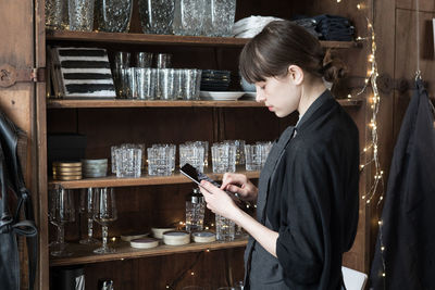 Side view of young female entrepreneur using digital tablet while standing by rack at store