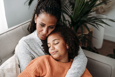 Mother embracing daughter relaxing on sofa at home