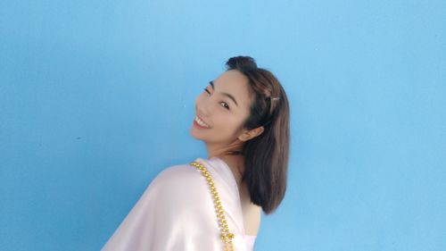 Side view portrait of smiling young woman winking against blue background