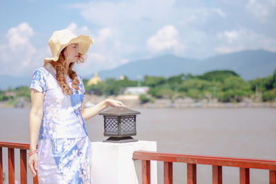 Woman standing by railing against sky