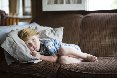 Full length of frightened boy lying on sofa at home