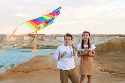 A girl watches as a boy deftly launches a kite into the sky.