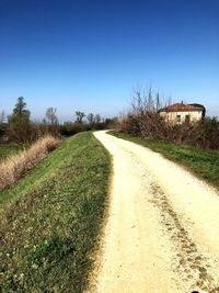 Empty road amidst field against clear blue sky