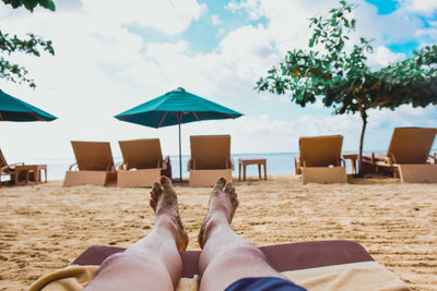 Low section of man relaxing at beach against sky