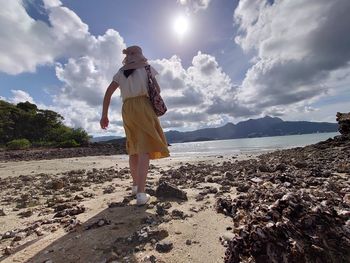 Rear view of woman standing on beach against sky